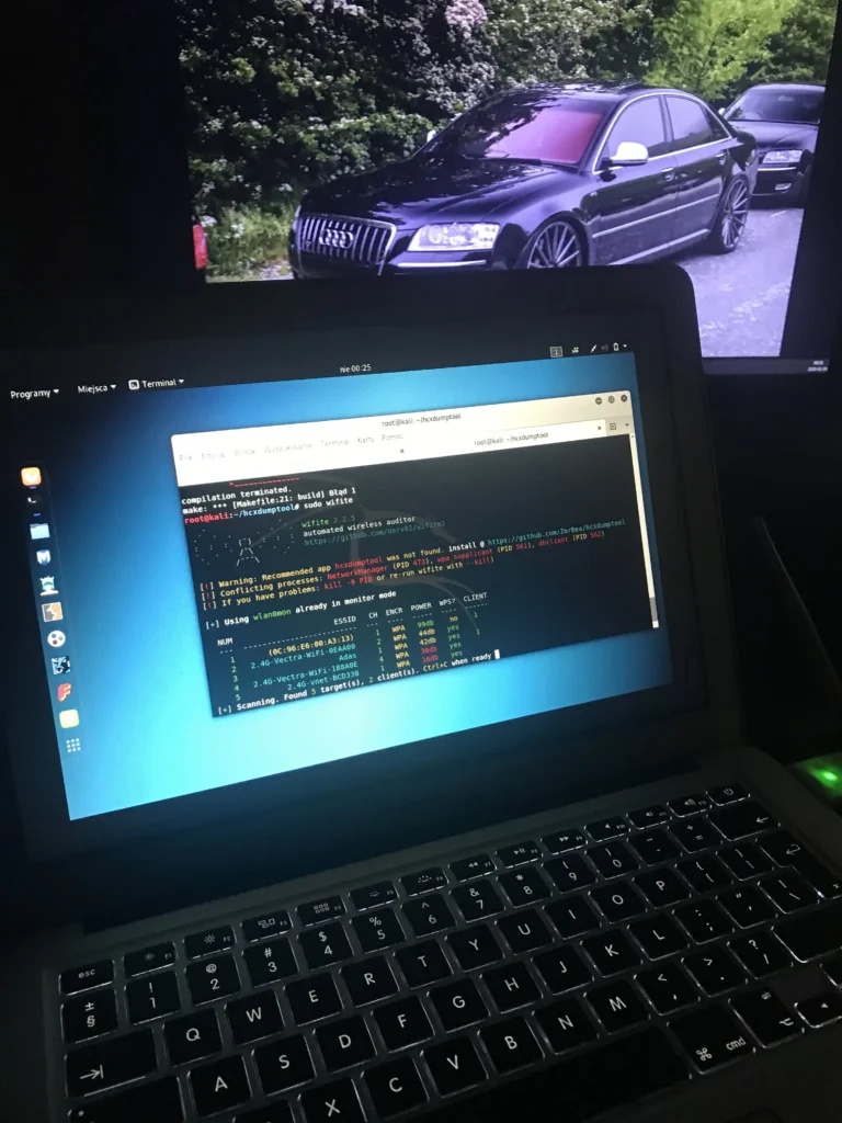 Ekran laptopa z systemem Kali Linux i otwartym terminalem; widoczny jest interfejs narzędzia do audytu sieci bezprzewodowych oraz lista wykrytych sieci.